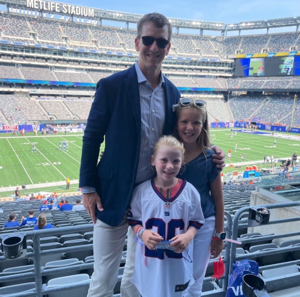 Eli Manning and two of his daughters at MetLife Stadium, smiling at the camera.