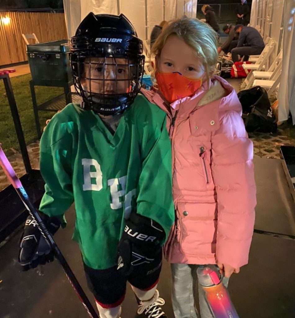 Eli Manning's kids, with one wearing a hockey mask and pads, and the other wearing a pink coat and face mask.