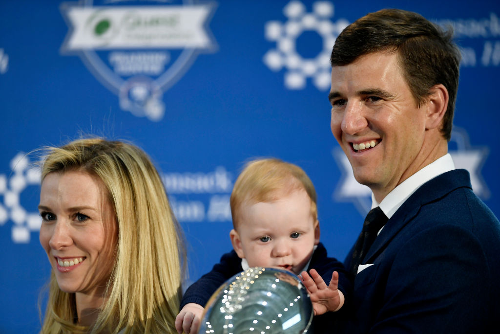 Eli Manning's child Charlie and his wife posing for cameras with a trophy.