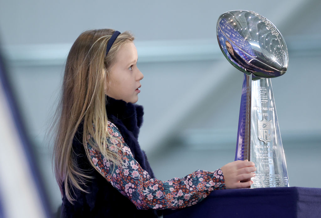 Eli Manning kid Lucy staring at a football trophy.