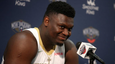 Fat Zion Williamson smiling as he speaks into a microphone at a press conference for the New Orleans Pelicans.