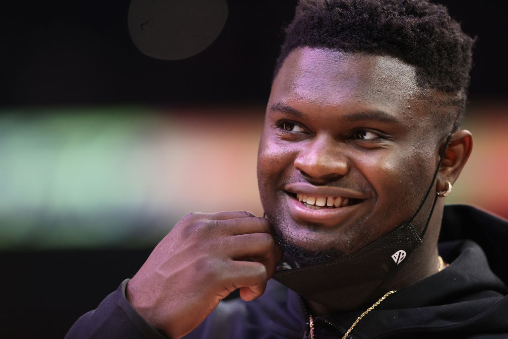 A close up image of Zion Williamson smiling and pulling down a black face mask.