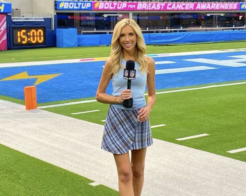 Justin Herbert Girlfriend Taylor Bisciotti reporting on a football field in a plaid skirt, holding a microphone.