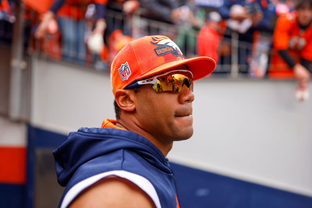 Russell Wilson looks on with Broncos hat on head