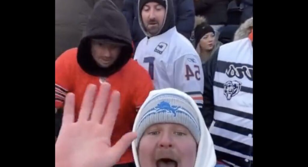 Lions fan waves to camera while taking selfie video with two Bears fans behind him.