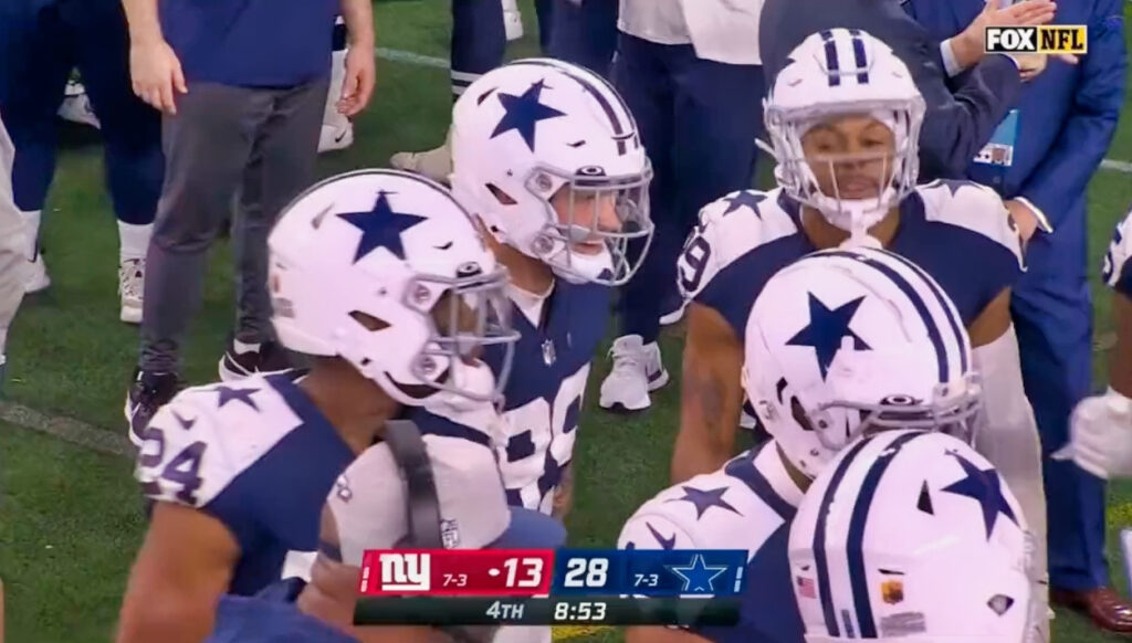 Cowboys players in a  huddle on sidelines