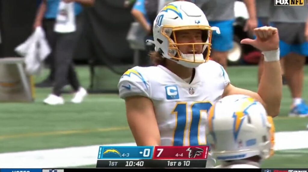 Chargers QB Justin Herbert points with his thumb over his shoulder.