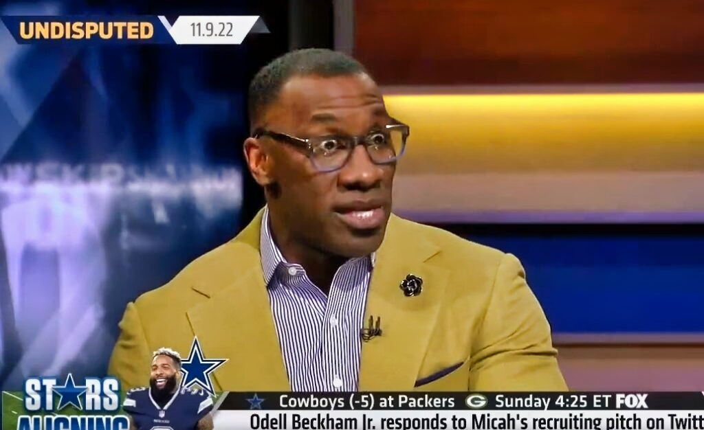 Shannon Sharpe in tan suit sitting at table
