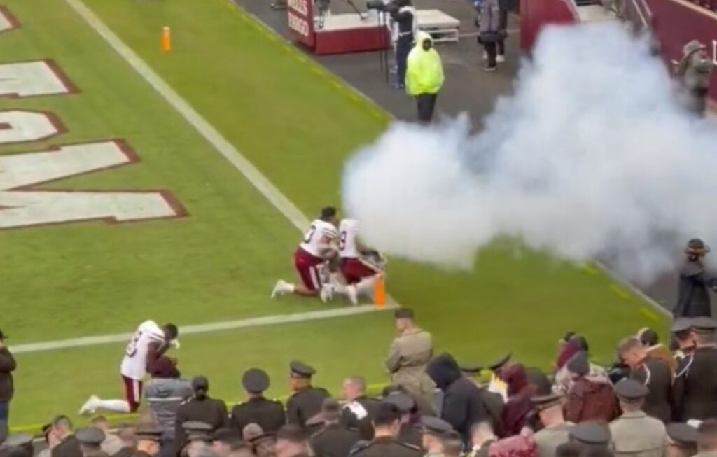 Players kneeling on field with smoke coming toward them