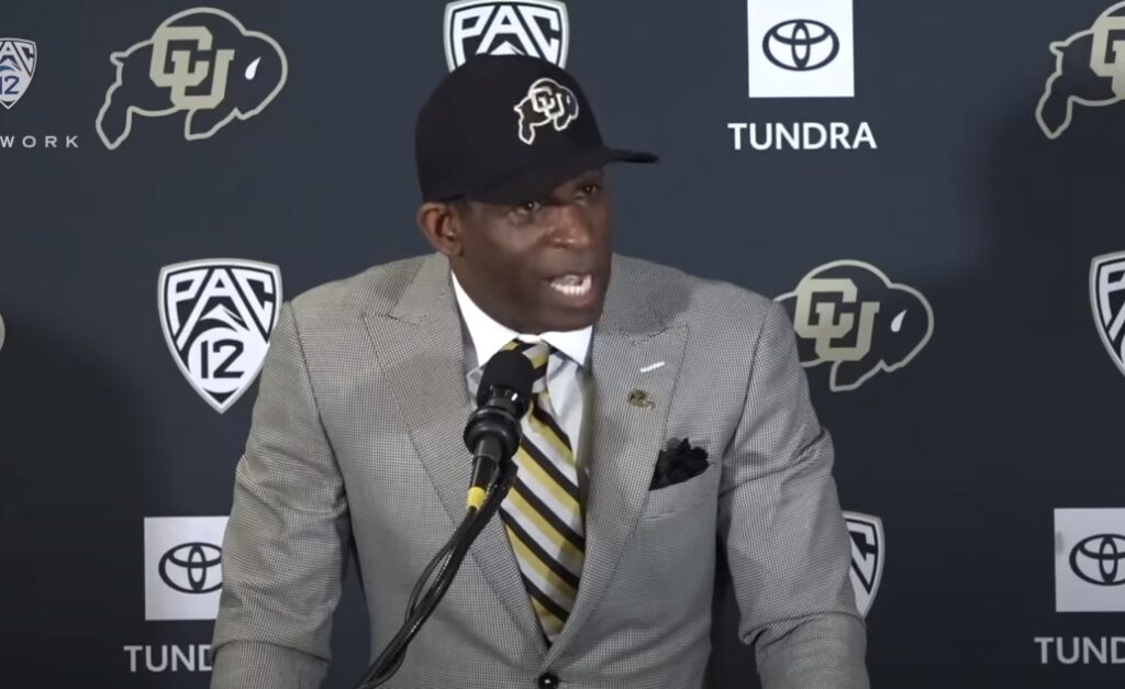 Deion Sanders in a suit at a podium