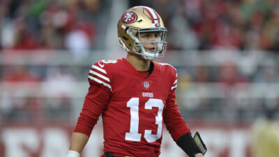 Brock purdy in a red San Francisco 49ers jersey with his helmet on in a game