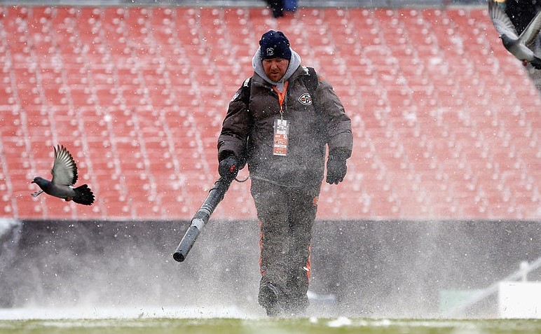 Cleveland Browns employee cleaning snow off the field at FirstEnergy Stadium.