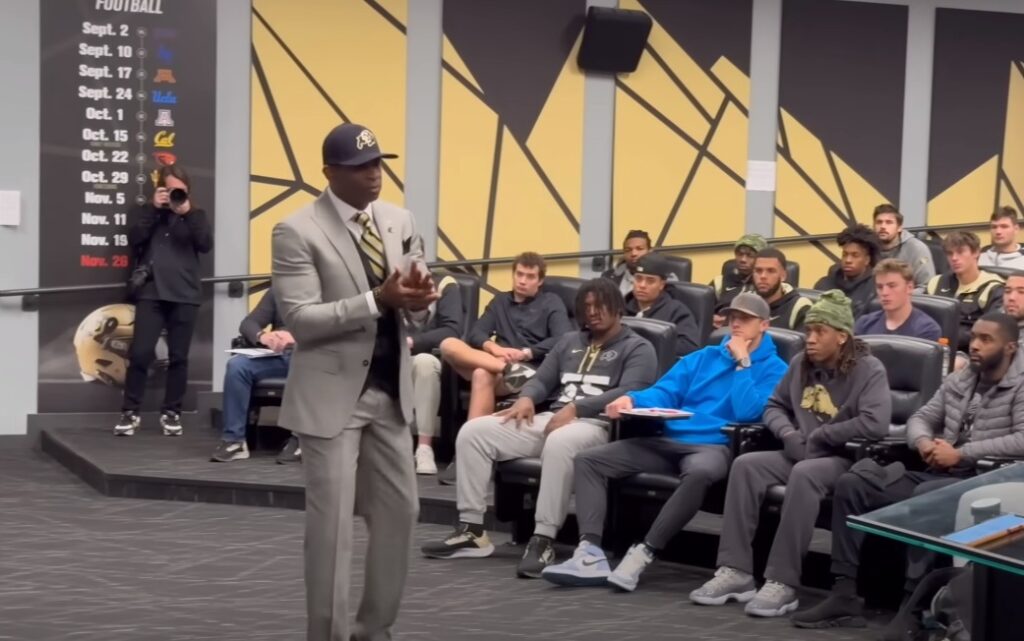 Deion sanders in a suit standing in front of a football team