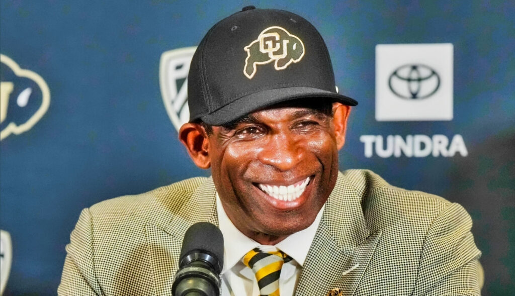 Colorado Buffaloes head coach Deion Sanders smiling at a press conference.