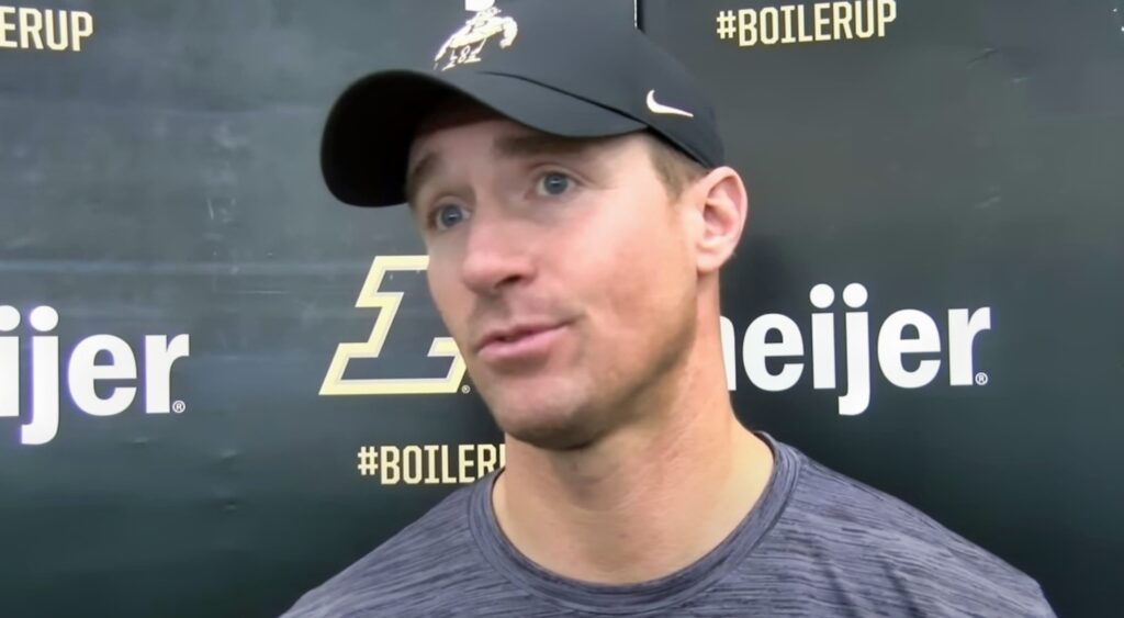 Drew Brees in a t-shirt and cap and speaking to reporters