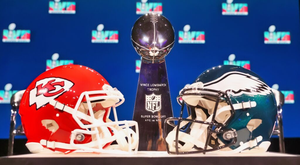 The Chiefs and Eagles helmets in front of the Lombardi Trophy on a table.