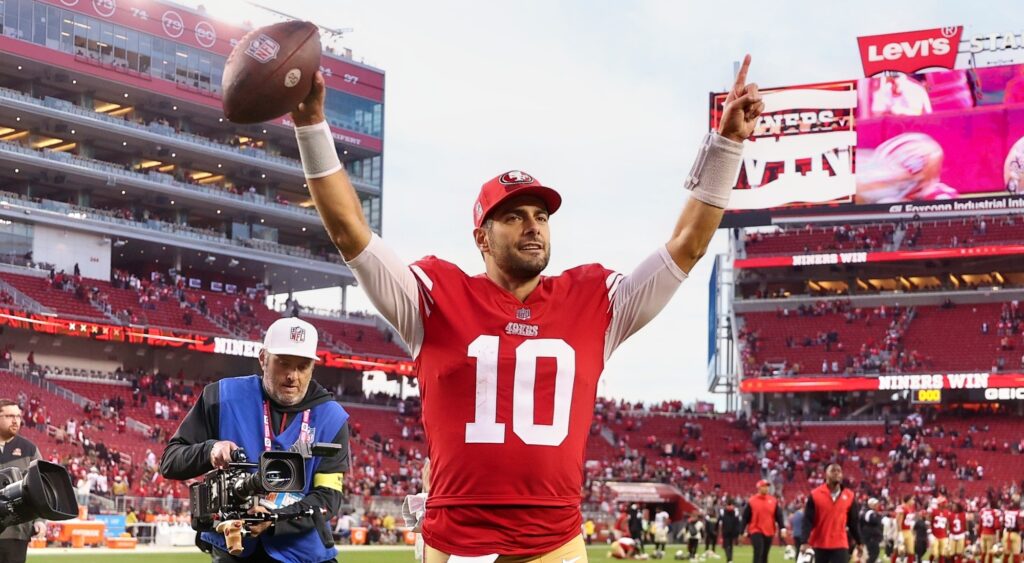 Jimmy Garoppolo holding a football in the air.