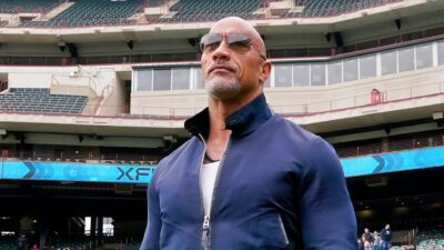 The Rock in sunglasses with XFL logo behind him inside stadium