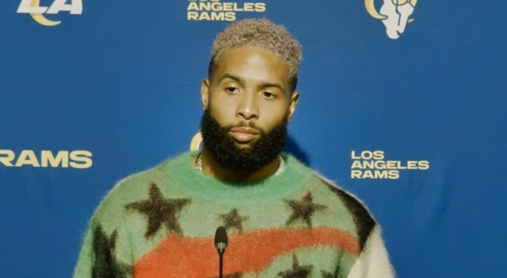 Odell at podium while wearing sweater