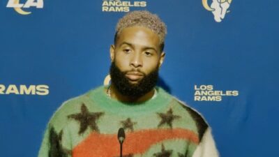 Odell at podium while wearing sweater