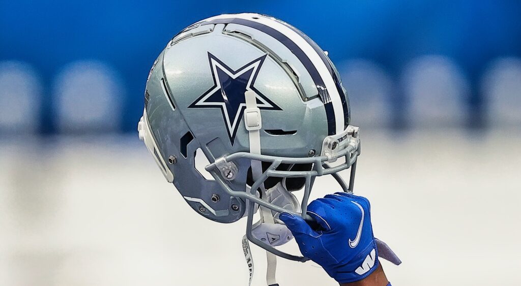 Dallas Cowboys player holds up his helmet with one hand.