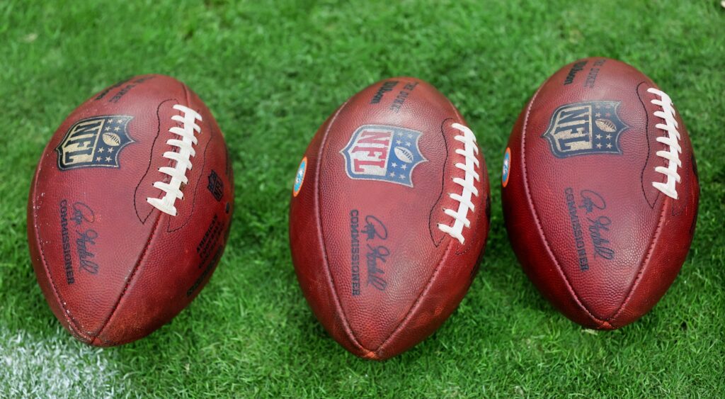 Three NFL footballs lined up on the grass.