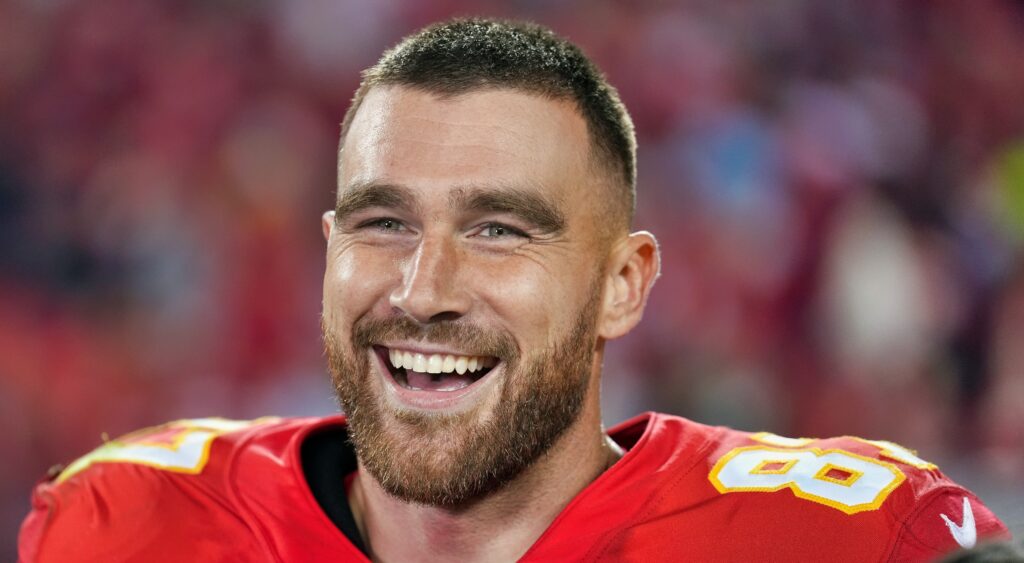 Travis Kelce smiles and looks on without his helmet.