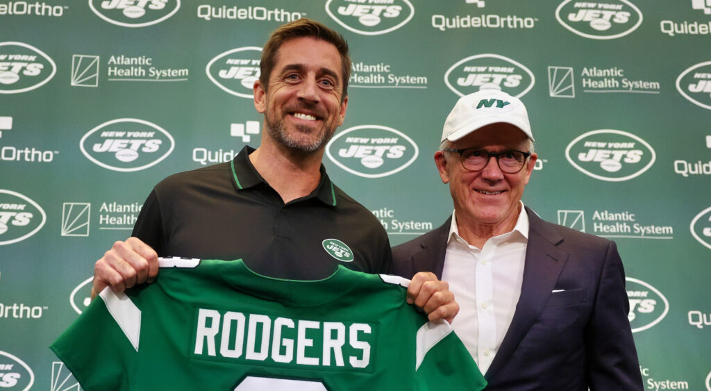 Aaron Rodgers holding his Jets Jersey while standing next to team owner Woody Johnson