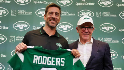 Aaron Rodgers holding his Jets Jersey while standing next to team owner Woody Johnson