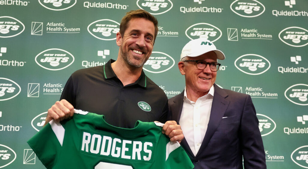 Aaron Rodgers holding up his Jets jersey alongside team owner Woody Johnson