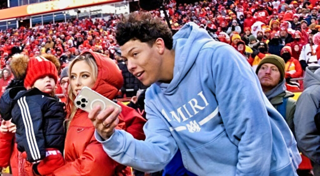 Jackson Mahomes holding cell phone while standing next to sister-in-law Brittany Mahomes