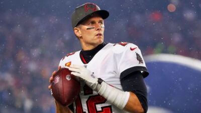 Tom Brady holding a football while wearing a cap