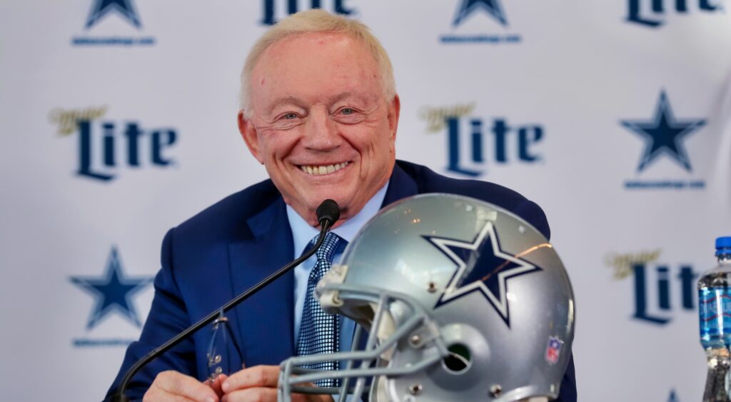 Jerry Jones speaks at a press conference in front of a Dallas Cowboys helmet.