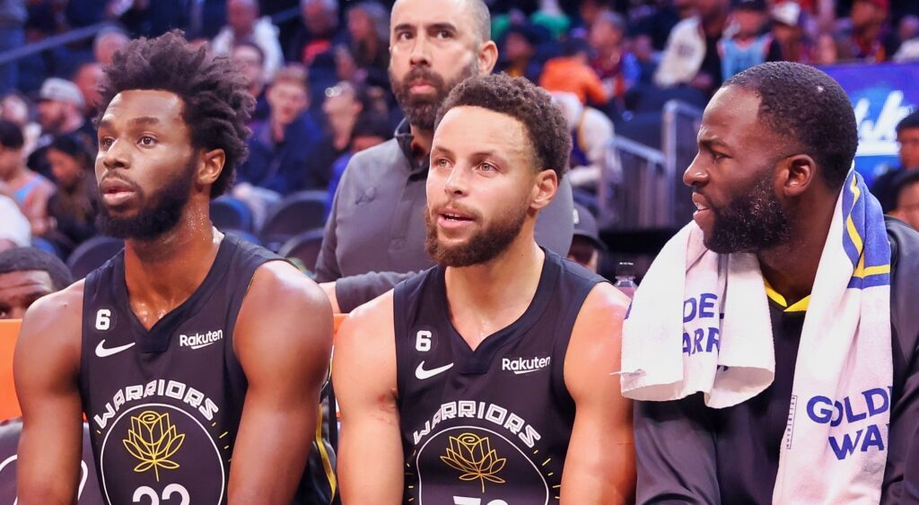 Andrew Wiggins, Stephen Curry and Draymond Green sitting on bench during game.