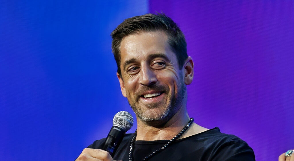 Aaron Rodgers smiling and holding a mic