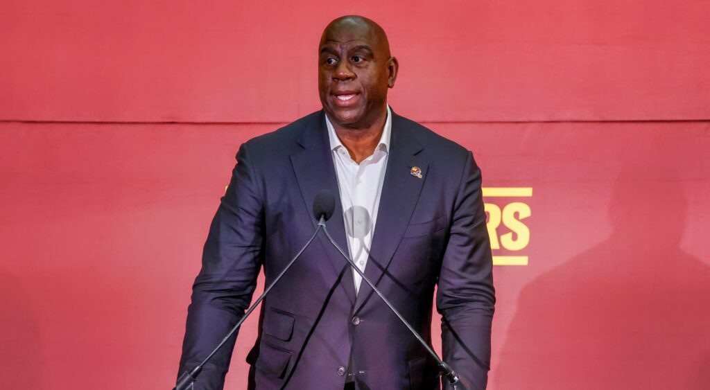 Magic Johnson speaking to reporters with commanders gear behind him