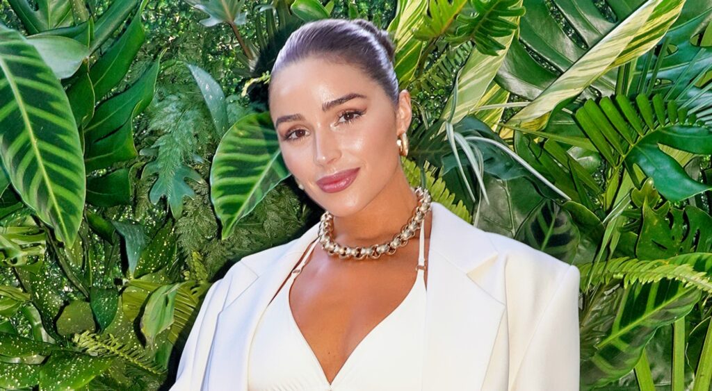 Olivia Culpo poses for a photo in front of greenery.