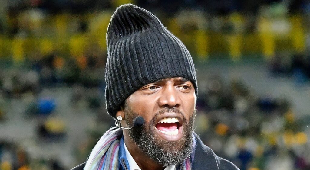 Former NFL wide receiver Randy Moss looking on.
