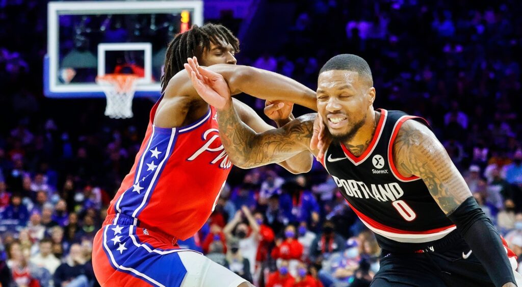 Damian Lillard (right) dribbling by Tyrese Maxey (left).