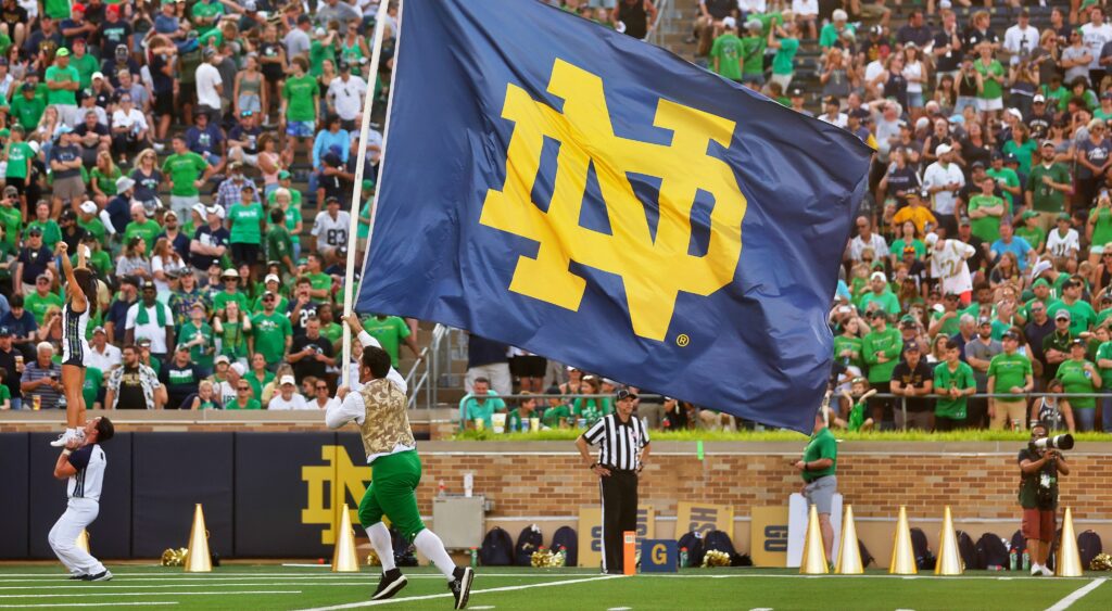 Notre Dame cheerleader runs onto the field with a flag.