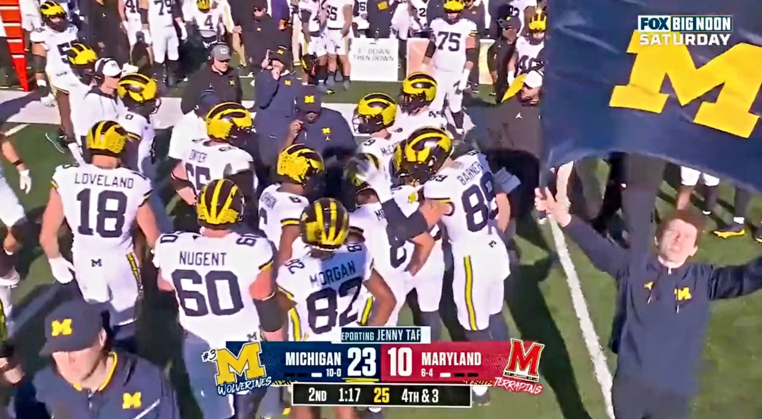 Michigan Wolverines players huddling on sideline.