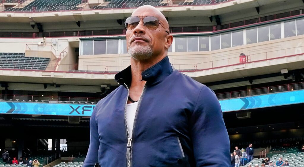 Dwayne Johnson looks on from the football field before an XFL game.