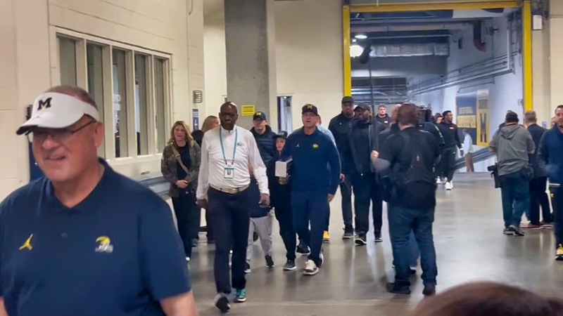 Jim Harbaugh and Michigan Wolverines staffers walking.