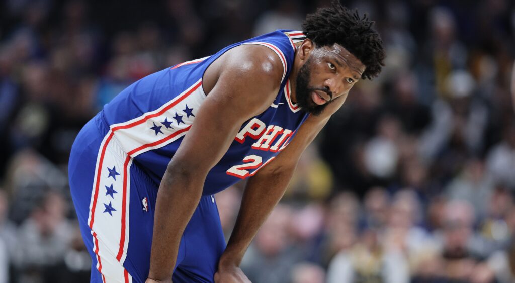Joel Embiid in 76ers jersey with his hands on his knees