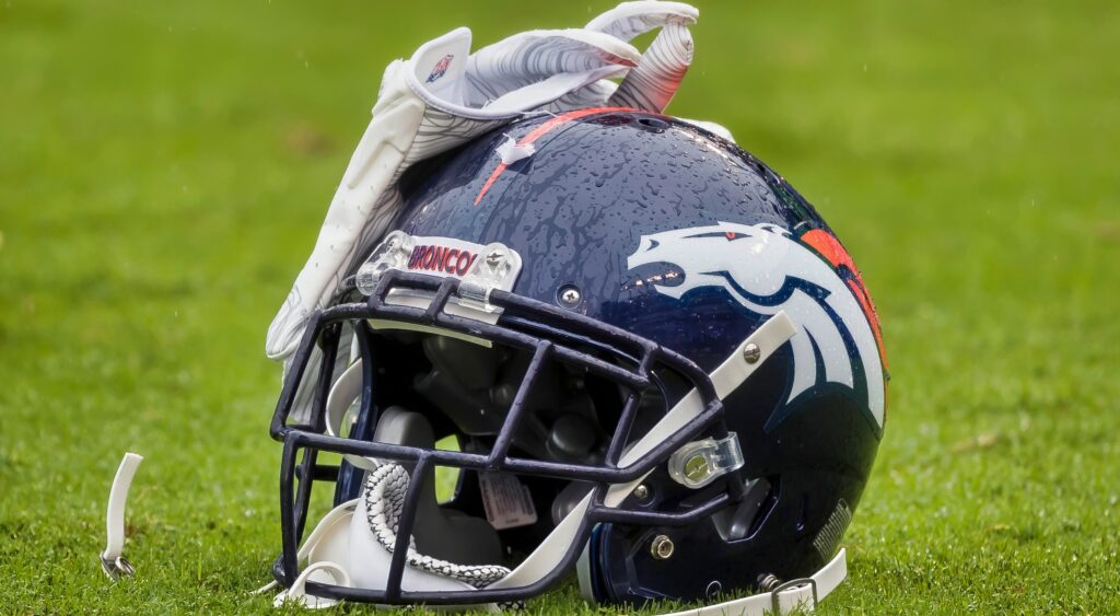 Denver Broncos helmet sitting on ground with a glove on top of it.