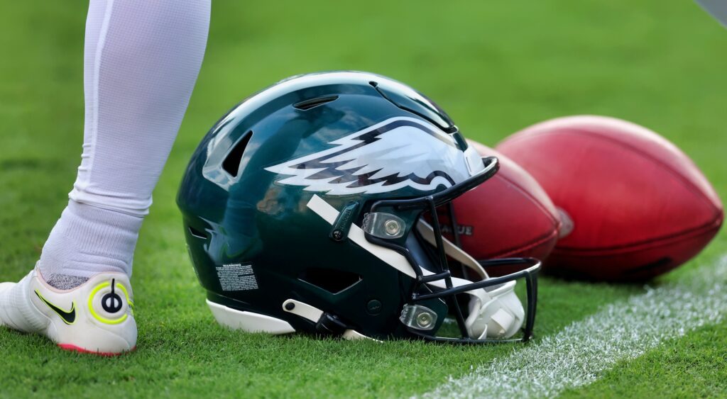 An Eagles helmet with a couple footballs on the field.