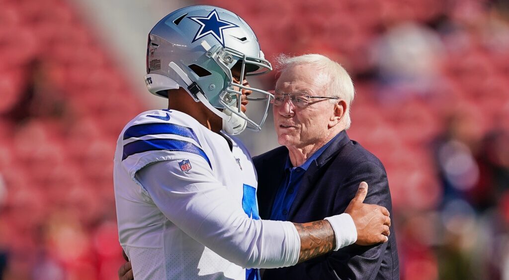 Dak Prescott and Jerry Jones embrace before a game on the field.