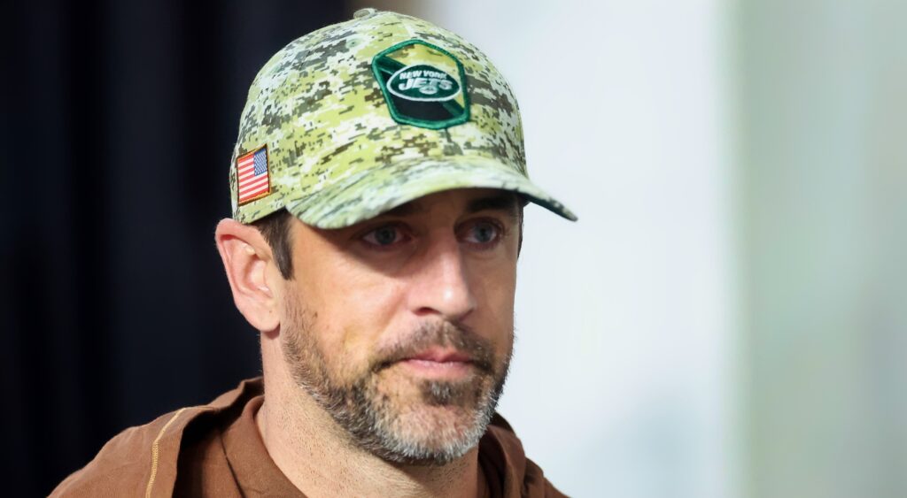 Aaron Rodgers looks on while wearing a Jets cap.