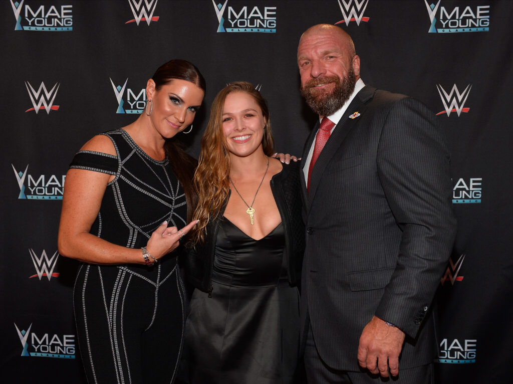 Ronda Rousey standing between Stephanie McMahon and Paul Levesque