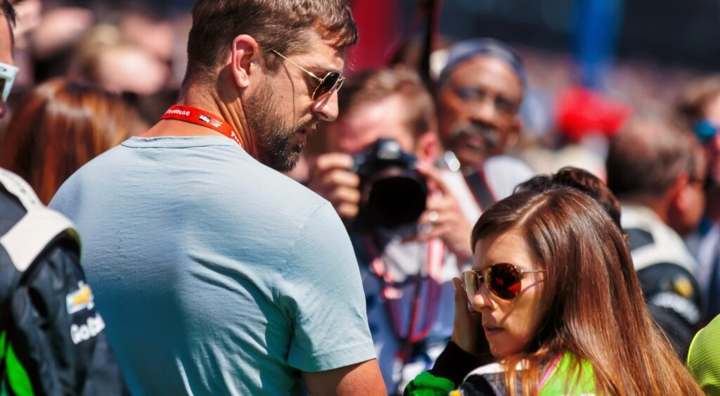 Danica Patrick in NASCAR gear and Aaron Rodgers loking at her.